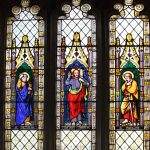 Three-light stained glass church window with brightly coloured saintly figures.