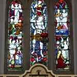 Three-panel stained glass window showing religious scenes in vivid colours.