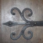 Ornate black wrought iron hinge on a wooden church door.