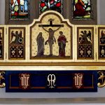 Decorated altar and reredos beneath stained glass in the church sanctuary.